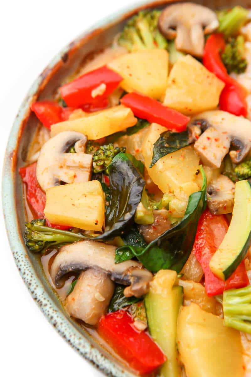 A close up of veggies in a red Thai curry sauce.