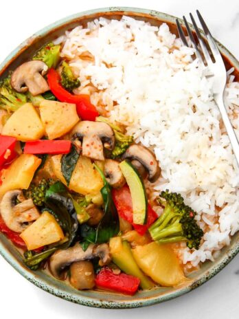 A top view of a plate filled with white rice and vegan red curry with vegetables and pineapple.