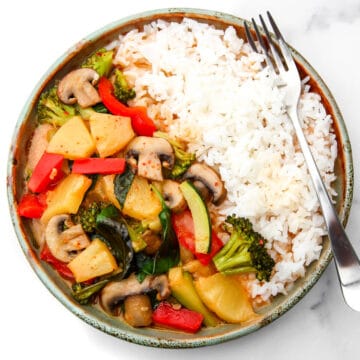 A top view of a plate filled with white rice and vegan red curry with vegetables and pineapple.