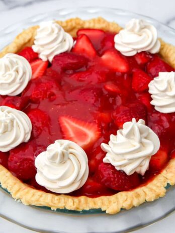 A top view of a strawberry pie topped with dollops of vegan whipped cream.