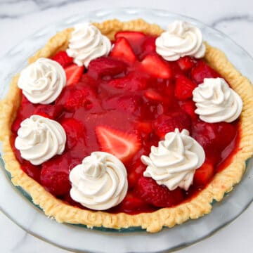 A top view of a strawberry pie topped with dollops of vegan whipped cream.