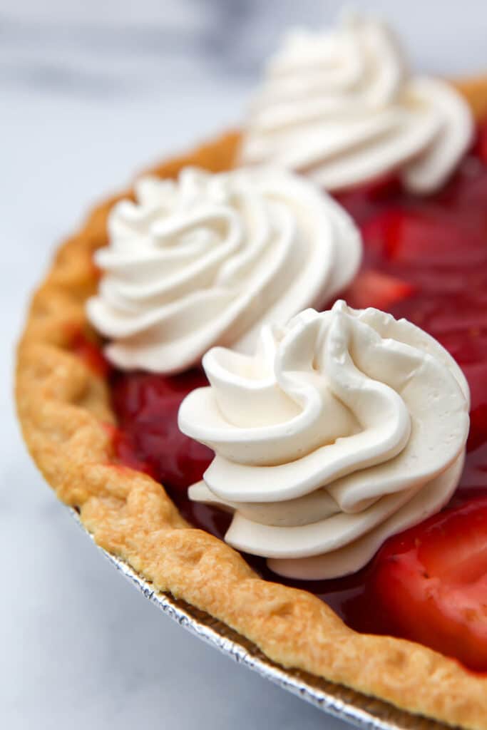 A close up of strawberry pie with vegan whipped cream on top.