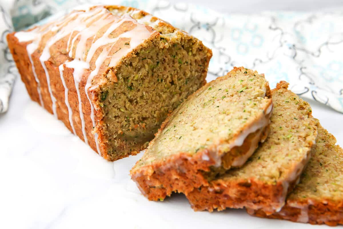 A loaf of egg free zucchini bread sliced with a tea towel behind it.