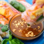 Vegan spicy peanut butter sauce in a small glass dish with a spring roll being dipped into it.