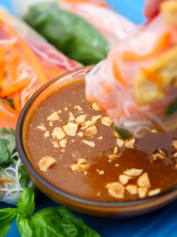 Vegan spicy peanut butter sauce in a small glass dish with a spring roll being dipped into it.