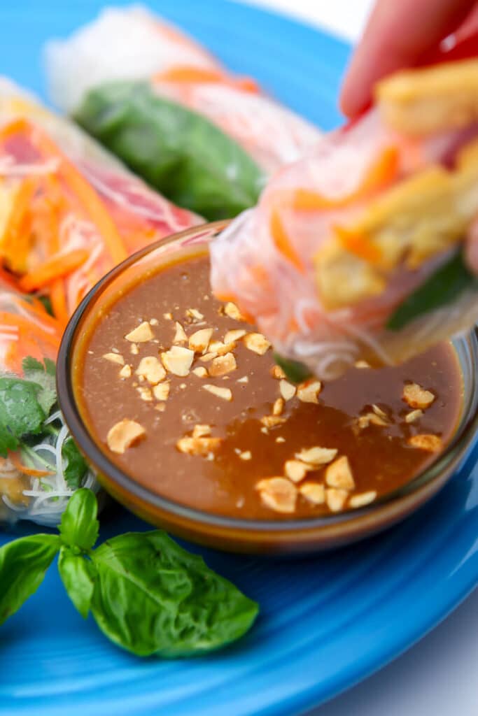 Vegan peanut sauce with a tofu spring roll being dipped into it.
