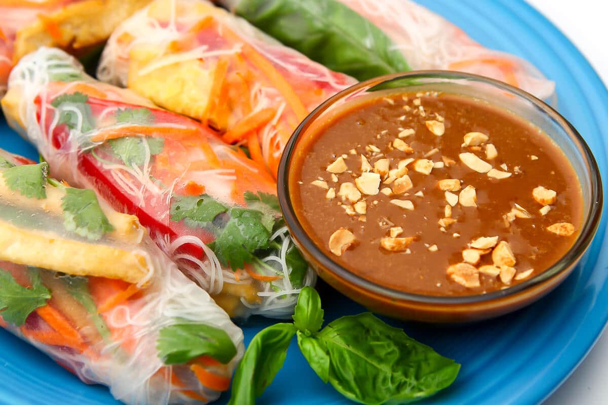 A close up of colorful veggies summer rolls with peanut dipping sauce on the side.