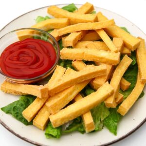 A white plate filled with tofu fries with a bowl of ketchup on the side.