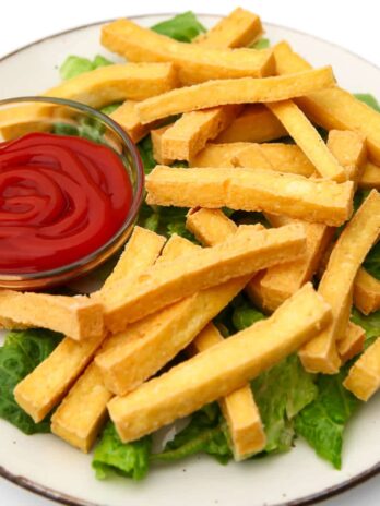 A white plate filled with tofu fries with a bowl of ketchup on the side.