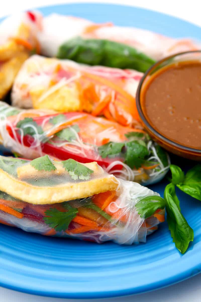 Vegan summer rolls filled with tofu, veggies, and fresh herbs on a blue plate.