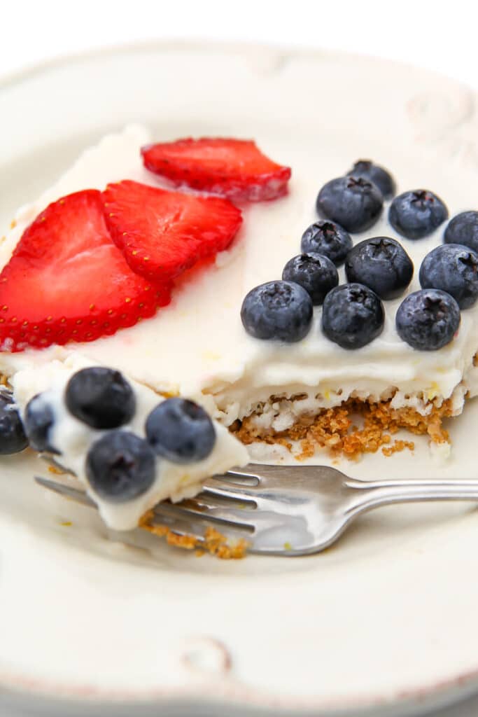 A slice of vegan ice cream cake with a crumb crust bottom and berries on top on  a white plate.