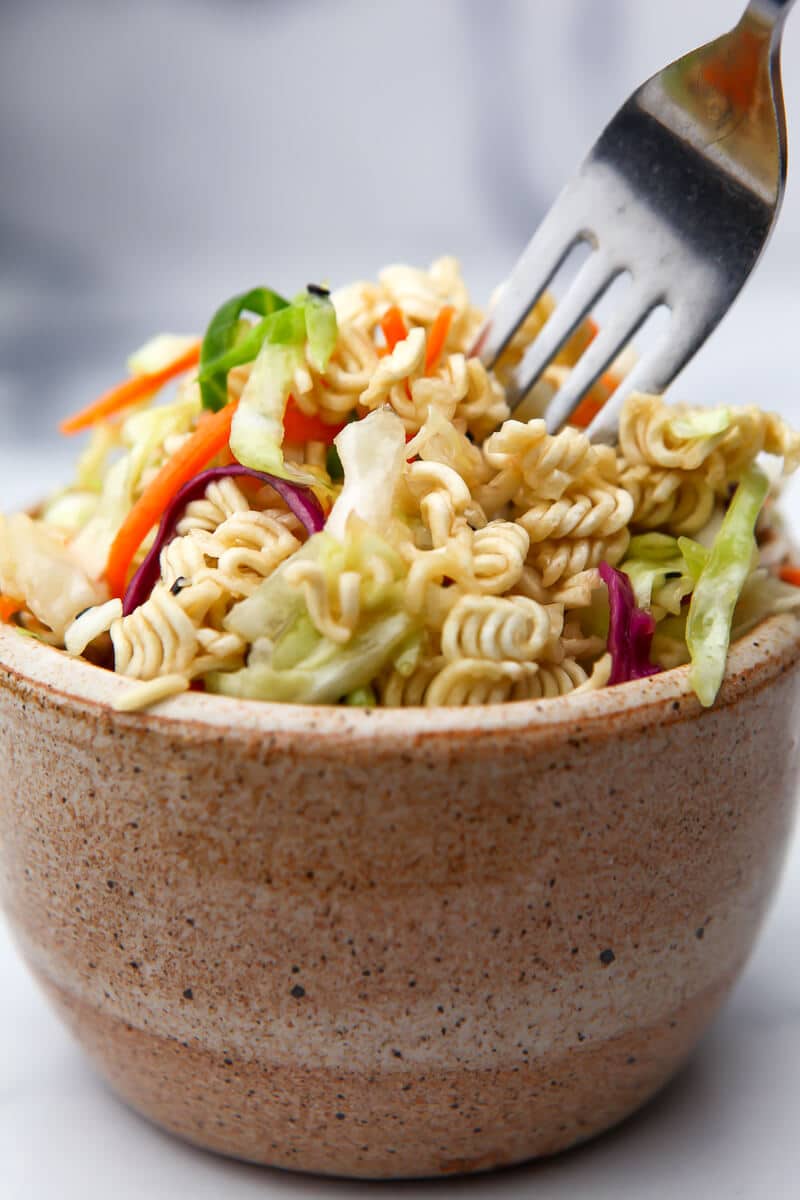 A bowl filled with ramen noodle salad with a fork in it.