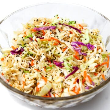 A glass bowl filled with vegan ramen noodle salad with cabbage and carrots and sprinkled with black sesame seeds.