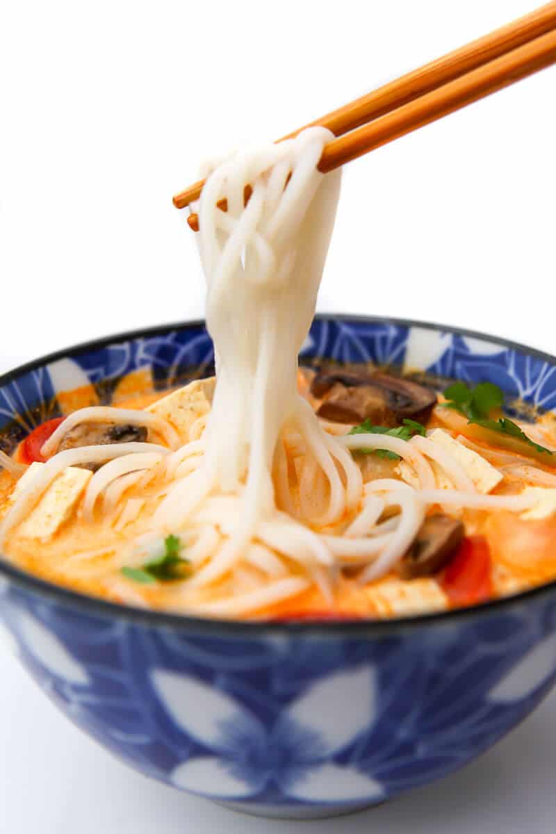 A bowl of vegan tom kha soup with chopsticks pulling up rice noodles.
