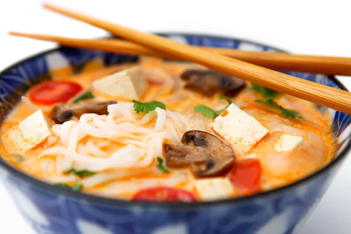 A blue bowl filled with spicy tom kha soup with a creamy coconut broth and tofu and mushrooms.