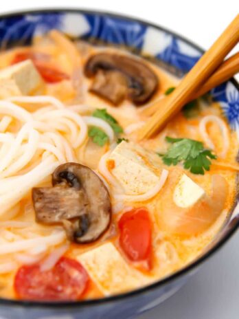 A blue bowl filled with creamy vegan tom kha soup with cherry tomatoes, tofu, mushrooms, and cilantro.