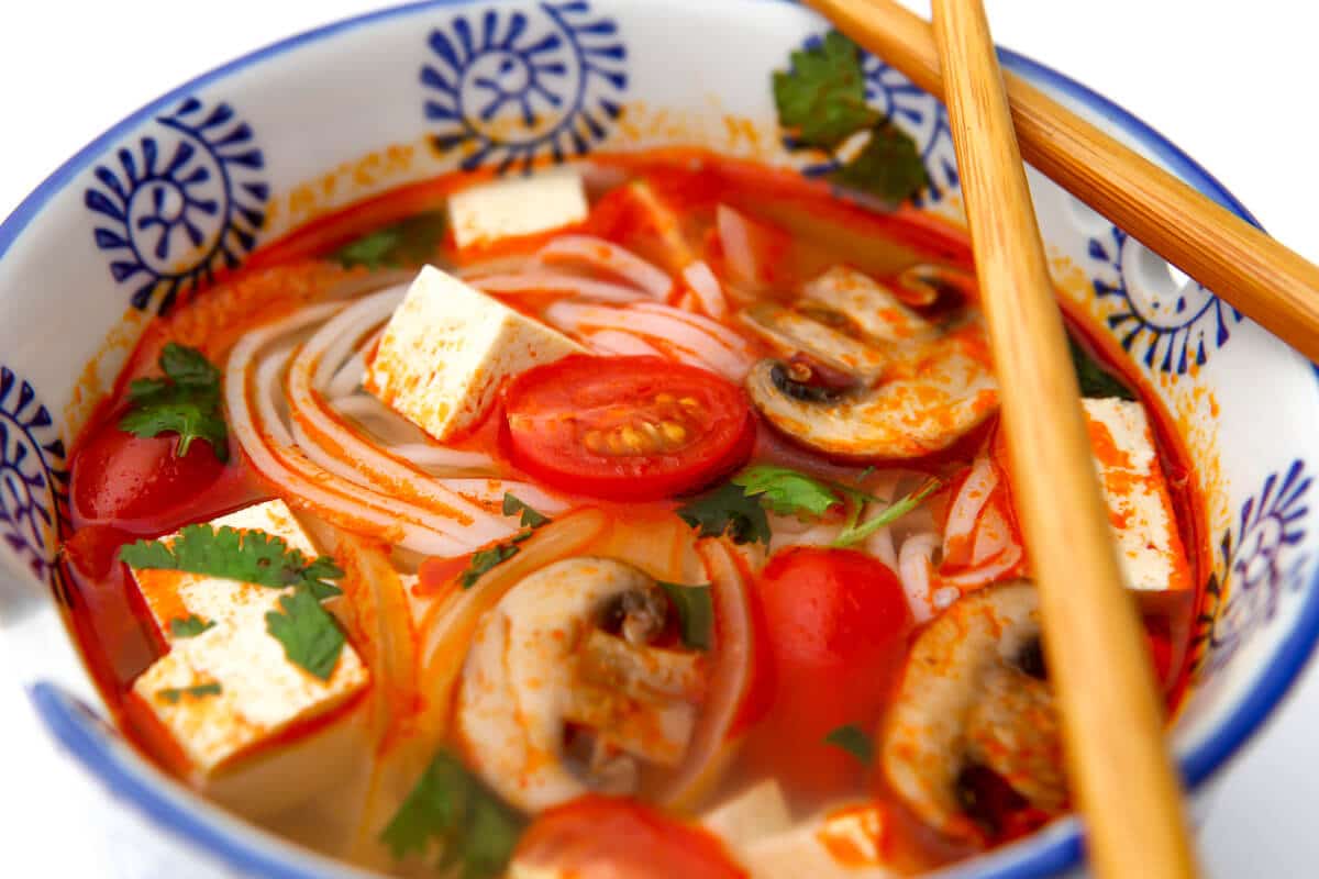 A bowl of vegetarian tom yum soup with veggies and tofu over rice noodles. 