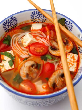 A top view of a bowl of vegan tom yum soup with chop sticks on top of the bowl.