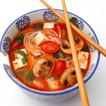 A top view of a bowl of vegan tom yum soup with chop sticks on top of the bowl.