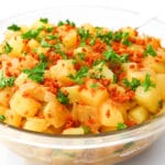 A large glass bowl filled with vegan German potato salad with bacon bits and parsley on top.