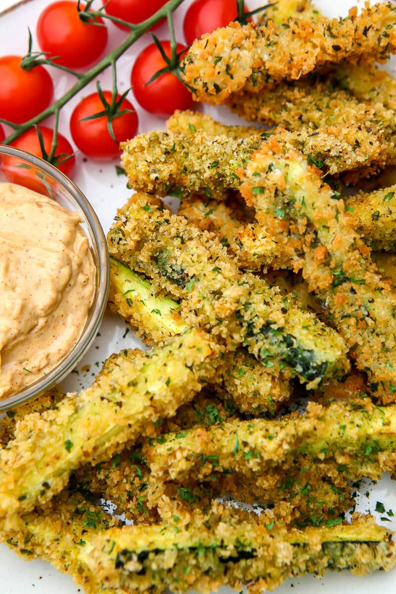 A close up of breaded vegan zucchini fries with chipotle mayo on the side.