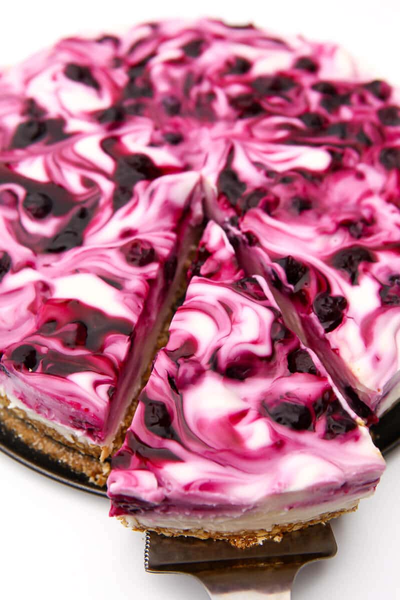 A slice being taken out of a swirly blueberry cheesecake.