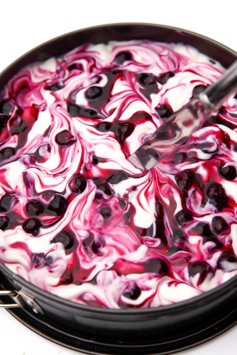 Blueberry sauce being swirled into a vegan cheesecake with a knife.