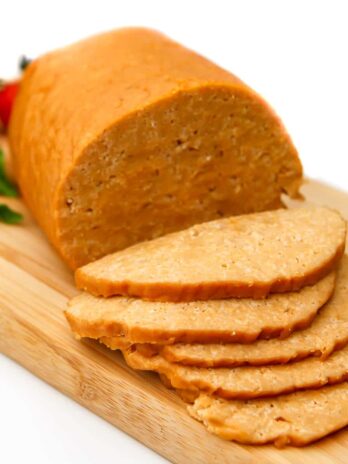 Vegan bologna on a cutting board with some slices of bologna in front of it.