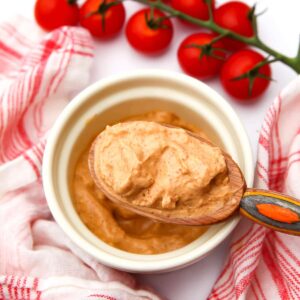 A large wooden spoon filled with vegan chipotle mayo with cherry tomatoes and a tea towel on the side.