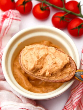 A large wooden spoon filled with vegan chipotle mayo with cherry tomatoes and a tea towel on the side.