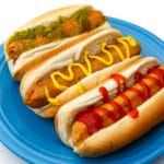 Three homemade vegan hot dogs with ketchup, mustard, and relish on them on a blue plate.
