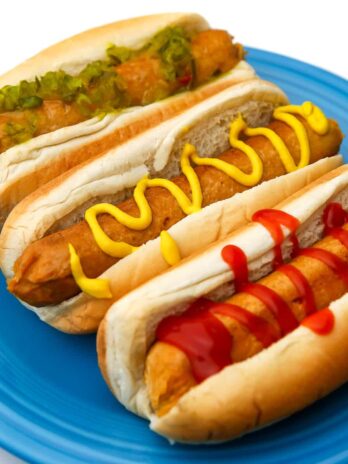 Three homemade vegan hot dogs with ketchup, mustard, and relish on them on a blue plate.