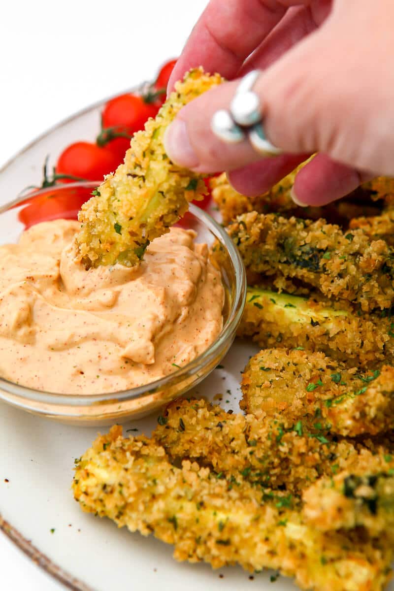 Someone dipping deep fried zucchini into a bowl of vegan chipotle mayo.
