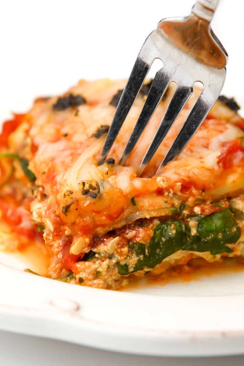 A piece of vegan zucchini lasagna with a fork sticking in it on a white plate.