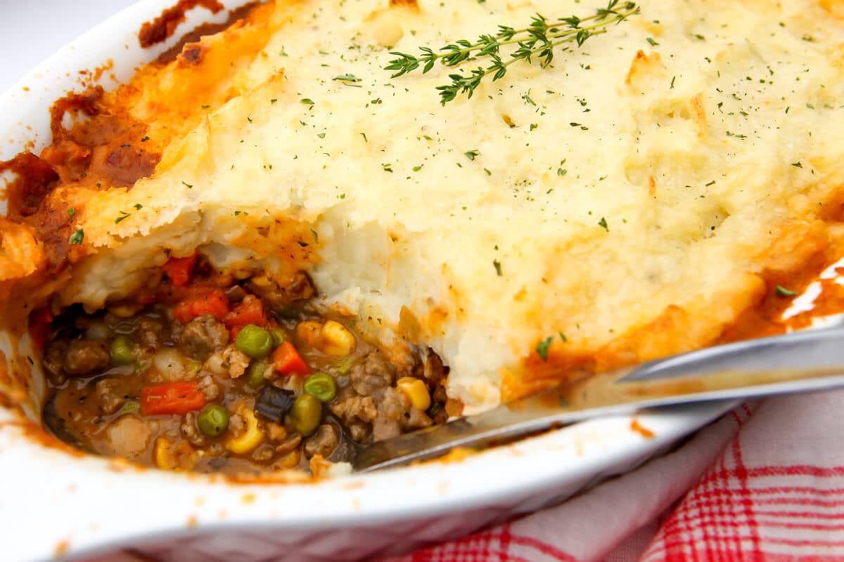 A close up of a vegan cottage pie in a white casserole dish with a scoop taken out.