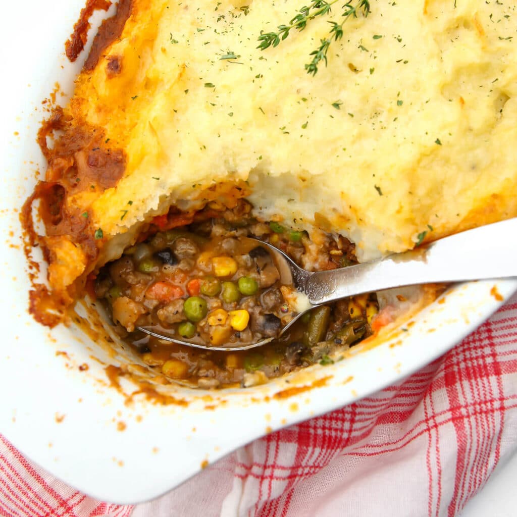 A top view of a white casserole dish filled with vegan shepherd's pie with a serving taken out.