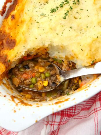 A top view of a white casserole dish filled with vegan shepherd's pie with a serving taken out.