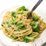 A white plate filled with vegan broccoli alfredo with a fork sticking in it.
