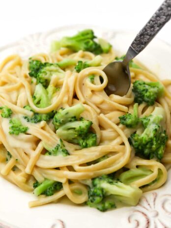A white plate filled with vegan broccoli alfredo with a fork sticking in it.