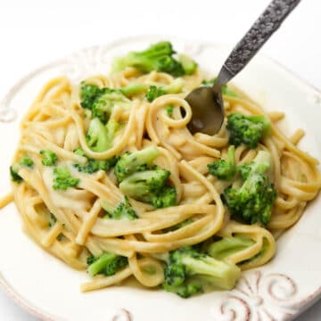 A white plate filled with vegan broccoli alfredo with a fork sticking in it.