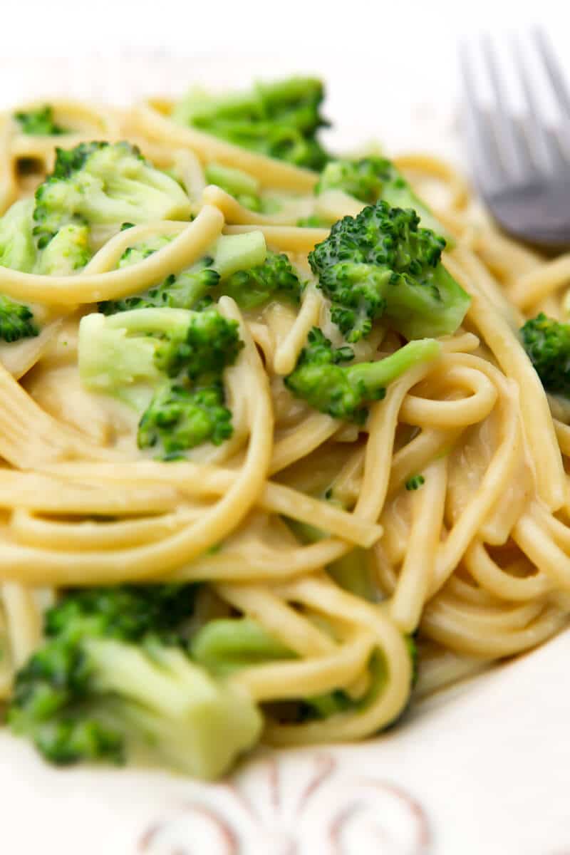 A close up of a plate full of vegan alfredo with broccoli over pasta.