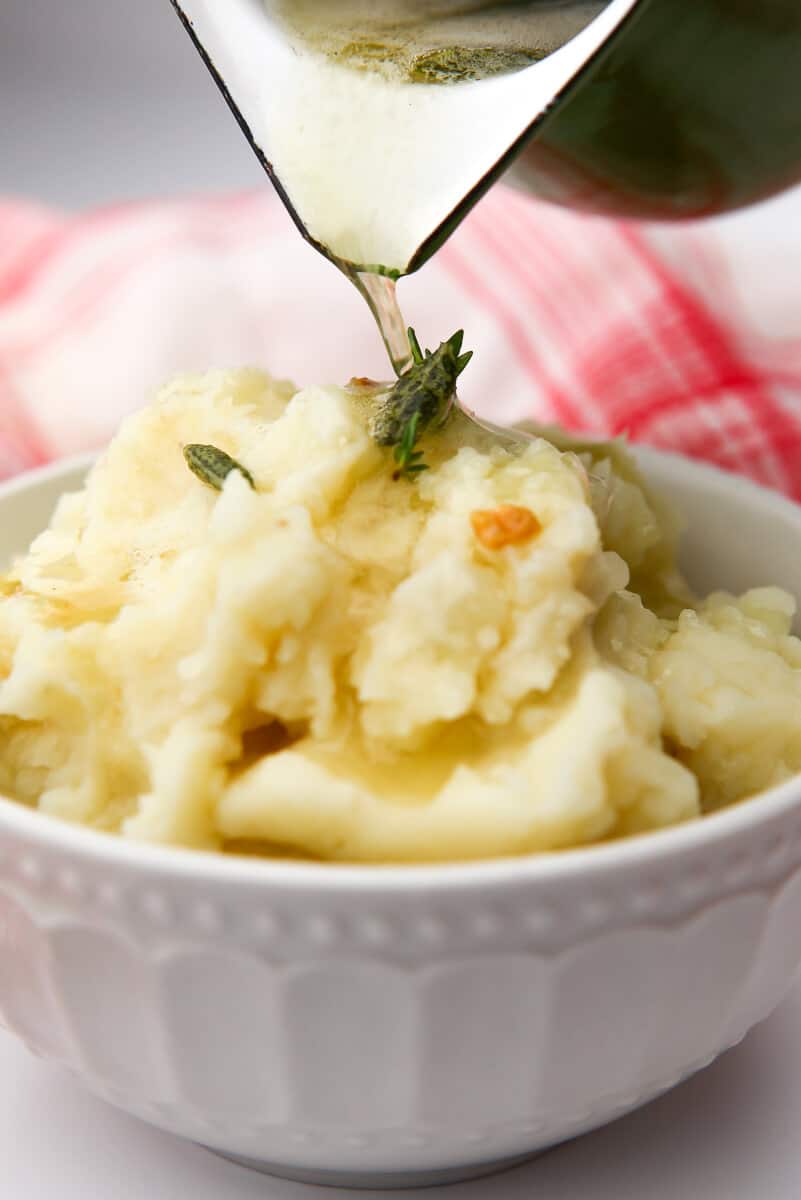 A white bowl filled with mashed potatoes with dairy-free brown butter being poured over top of it.