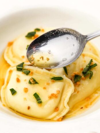 A white bowl with perogies in a brown butter sauce with garlic and sage.
