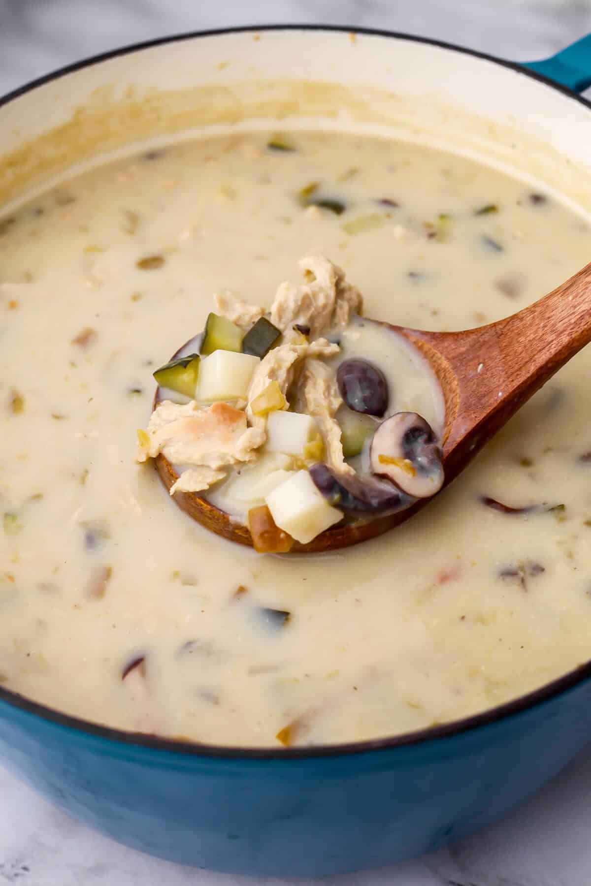 A large pot of vegan green chile stew with a wooden ladle scooping up some.