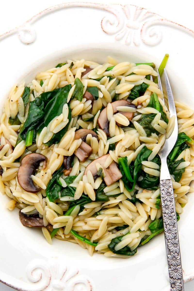 A white bowl filled with vegan orzo with mushrooms, spinach, and lemon.