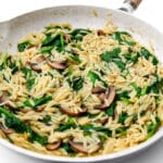 A white frying pan filled with vegan orzo with mushrooms and spinach.