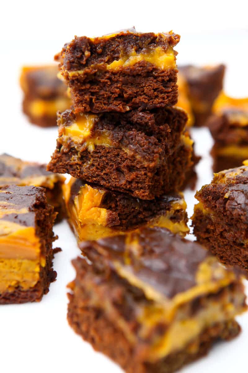Vegan pumpkin brownies with pumpkin swirled in them stacked up in a tower of 3 with more brownies around it.
