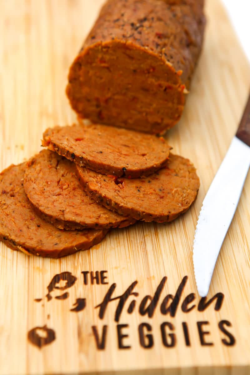 Vegan seitan salami sliced on a cutting board with a knife on the side.