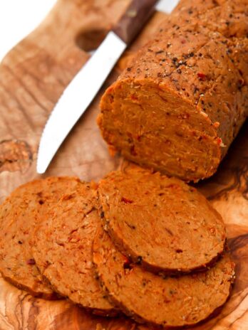 Vegan salami sliced on a cutting board with a knife next to it.