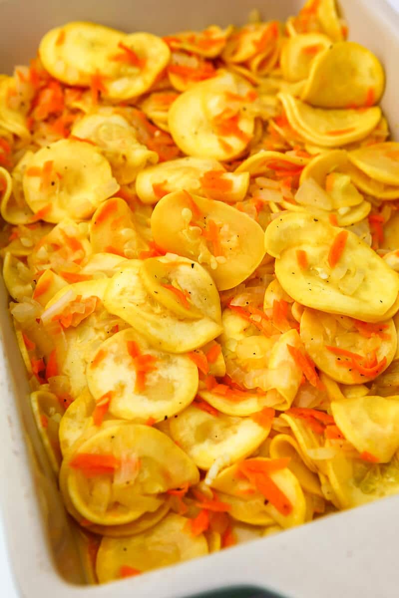 Sauted yellow squash, onions, and shredded carrots in a casserole dish.